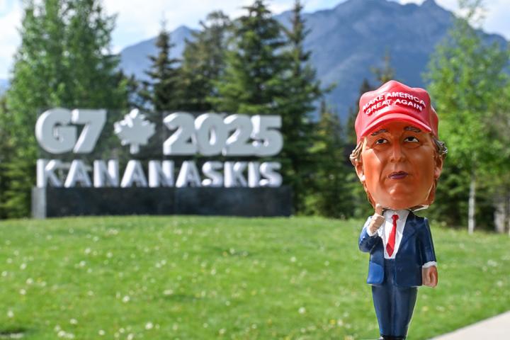 Una figura que representa a Trump frente al cartel que indica la celebración de la reunión del G-7
