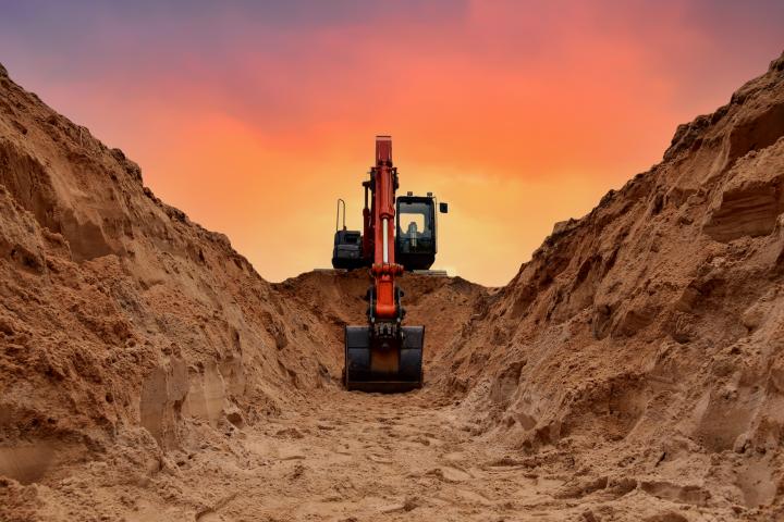 Excavadora excava zanja en el fondo de la puesta de sol.