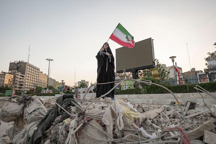 Una estudiante de arte iraní, con velo, ondea la bandera de su país sobre los escombros de un edificio destruido en Teherán