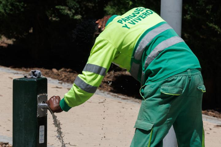 Un trabajador del equipo de Parques y Jardines de Madrid se refresca en una fuente.