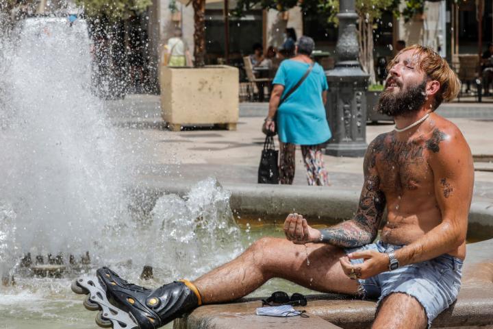 Un hombre se refresca en una fuente, en una fotografía de archivo
