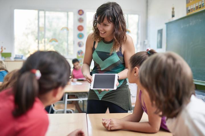 Una profesora muestra una tablet a sus alumnos durante una clase en primaria. El uso de tecnología en las aulas sigue generando debate entre docentes, familias y autoridades educativas.