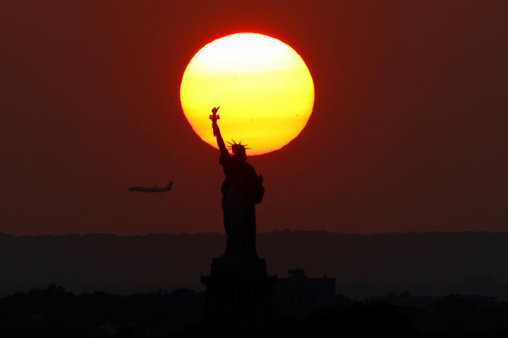 Un avión ante un atardecer con la Estatua de la Libertad de fondo, en Nueva York (EEUU).