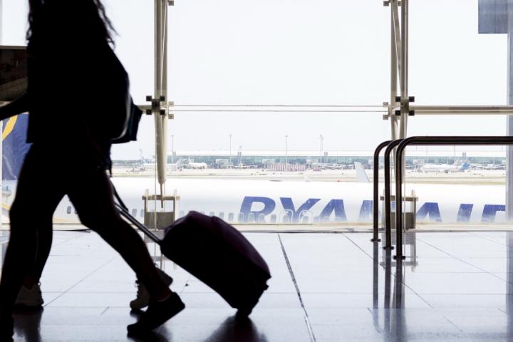 Un pasajero con su equipaje de mano en el aeropuerto, con un avión de Ryanair al fondo