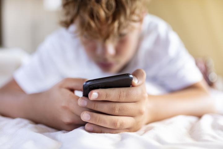 Un adolescente consulta su teléfono móvil tumbado en la cama.