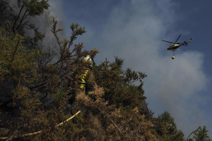 Un helicóptero de la lucha contra el fuego vuela sobre un bombero que trabaja en la extinción del incendio de la parroquia de A Cova (Lugo) el 22 de agosto.