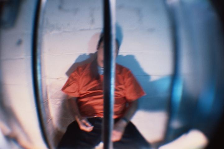 Preso con uniforme naranja sentado en una celda, símbolo del fallo judicial por la videoconsola dañada en prisión.