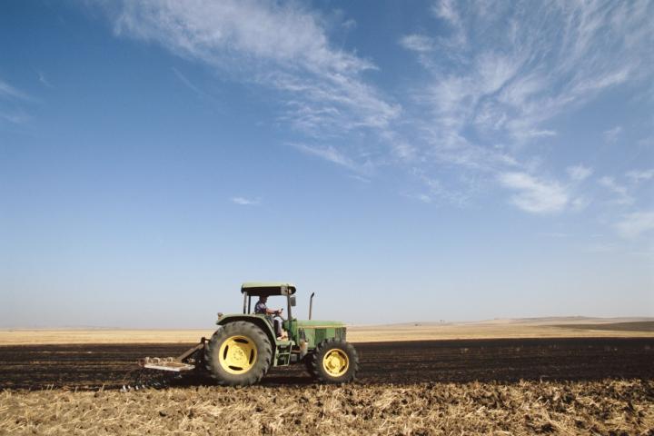 Tractor verde arando un campo bajo un cielo despejado.