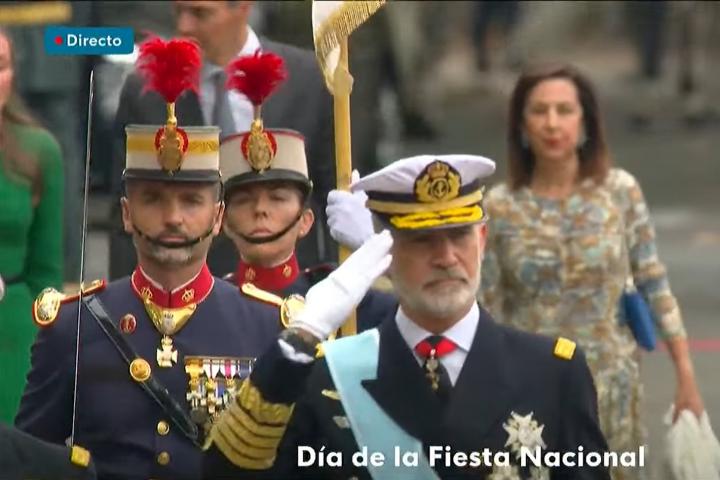 Felipe VI pasando revista y, detrás, la reina Letizia hablando con Pedro Sánchez