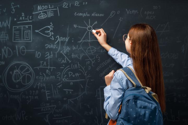 Una adolescente en clase escribiendo en una pizarra.