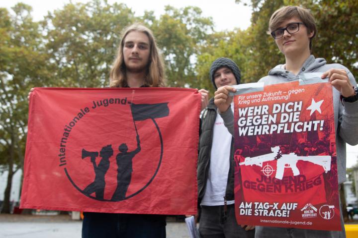 Tres jóvenes sujetan pancartas de protesta contra los planes de reintroducir el servicio militar en Colonia, Alemania.