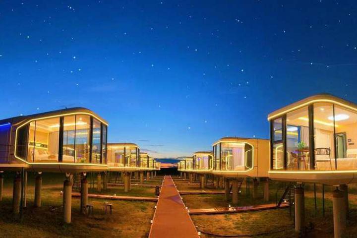 Conjunto de casas cápsula futuristas iluminadas por la noche, con estructura elevada y grandes ventanales de vidrio.