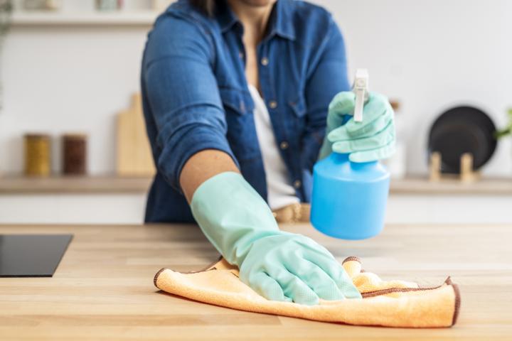 Ama de casa limpiando la encimera de madera de la cocina con un spray desinfectante y un paño.
