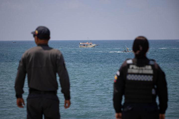 Agentes de la Policía de Venezuela vigilan la costa de La Guaira, con un barco al fondo, en el mar.