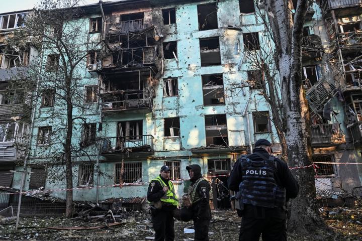 Cráter negro en un edificio residencial de Zaporiyia, atacado por Rusia, mientras agentes de policía montan guardia en los alrededores.