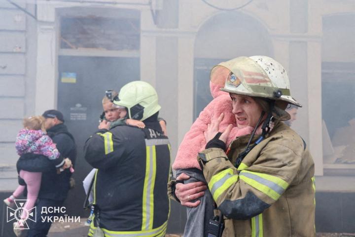 Bomberos y rescatistas abrazan a unos niños ucranianos rescatados de una guardería tras un ataque ruso con drones.
