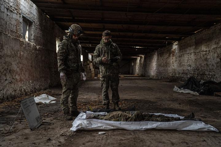 Dos voluntarios con atuendo militar tratan de identificar el cuerpo de un soldado ruso muerto en Ucrania.