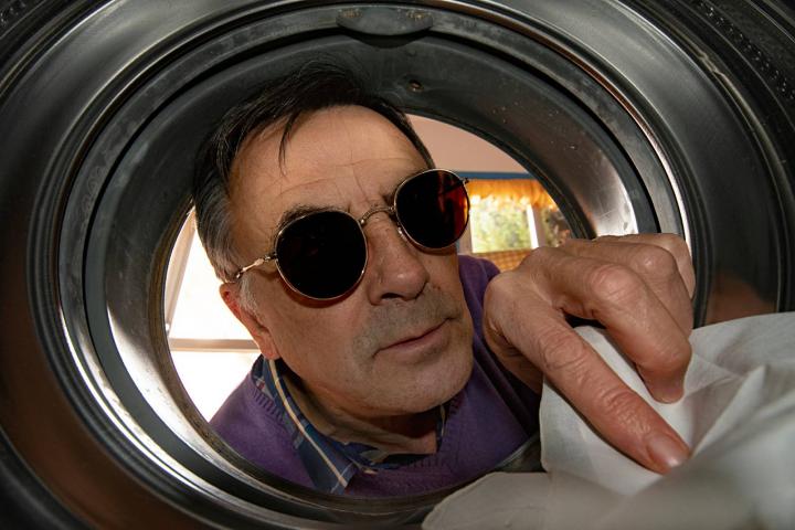Un hombre con gafas de sol observa con curiosidad el interior de la lavadora