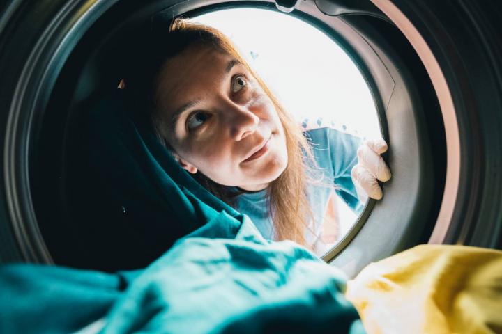 Una mujer con guantes observa el interior de una lavadora