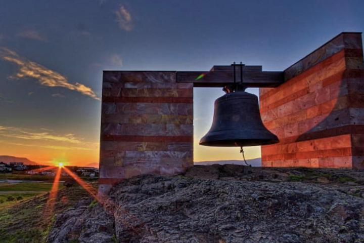 Una campana en medio del campo con un atardecer de fondo