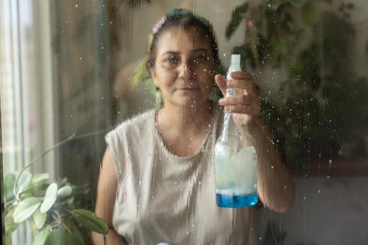 Mujer limpiando y secando la ventana con una botella de spray