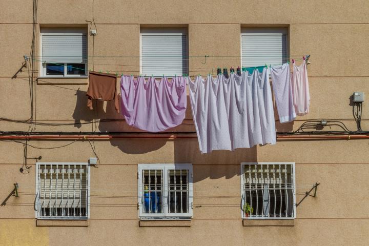Ropa y sábanas tendidas al sol en la fachada de un edificio residencial.