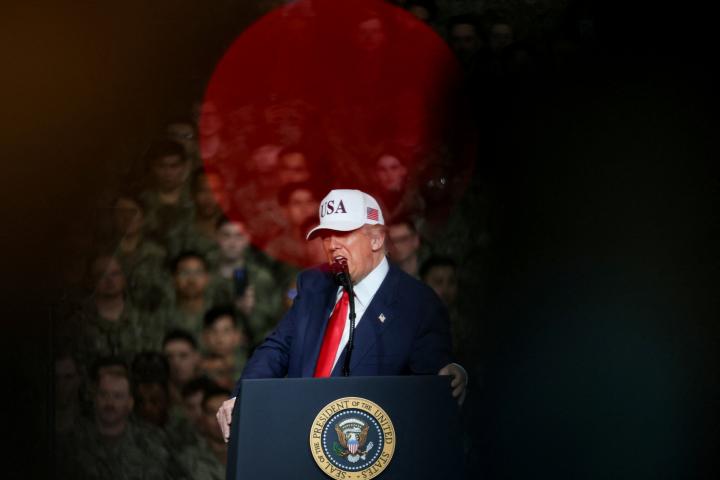 La luz roja de una cámara ilumina a Donald Trump, con gorra, mientras habla a los soldados norteamericanos en misión en Japón.