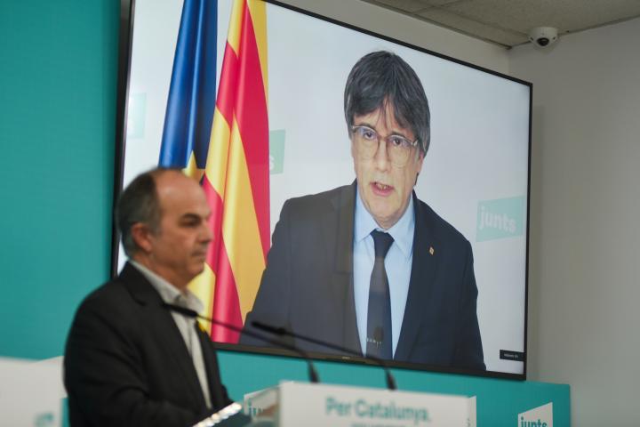 El secretario general de Junts, Jordi Turull, con el expresident catalán Carles Puigdemont, de fondo en la pantalla.