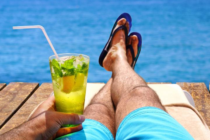 Hombre relajándose en la tumbona y tomando el sol con una bebida de mojito frío en el muelle de playa de madera