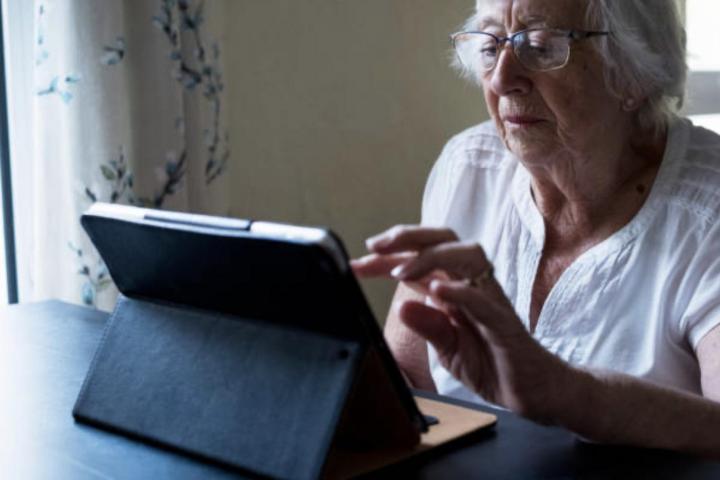 Primer plano de una mujer mayor sentada en una mesa usando la pantalla táctil de una tablet digital.