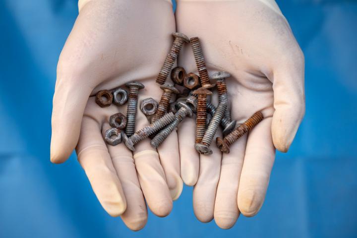 Primer plano de unas manos sosteniendo tornillos oxidados.
