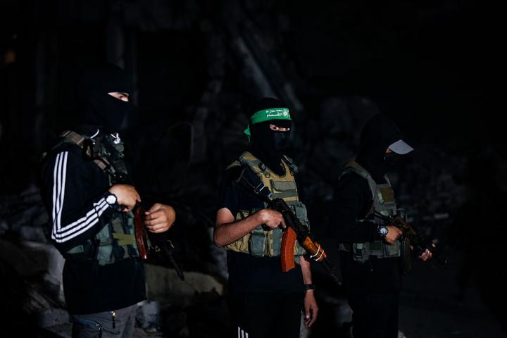 Miembros enmascarados de las Brigadas Ezzedin Al-Qassam, el brazo armado de Hamás, vigilan la entrega de cuerpos de rehenes a Cruz Roja, en mitas de la noche.