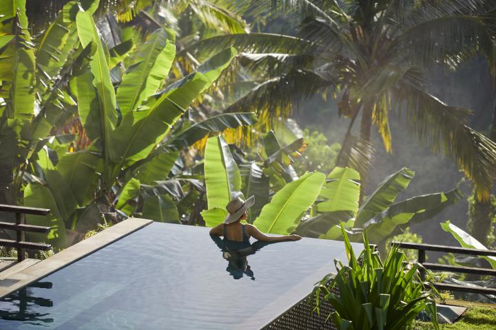 Mujer disfrutando de una hermosa piscina privada en una villa de lujo en Ubud (Bali, Indonesia), rodeada de árboles y plantas tropicales, situada al borde de un valle brumoso.