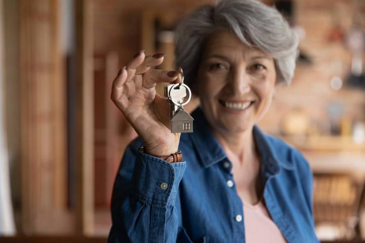 Una mujer mayor sosteniendo las llaves de casa con un divertido adorno en el llavero en forma precisamente de casa