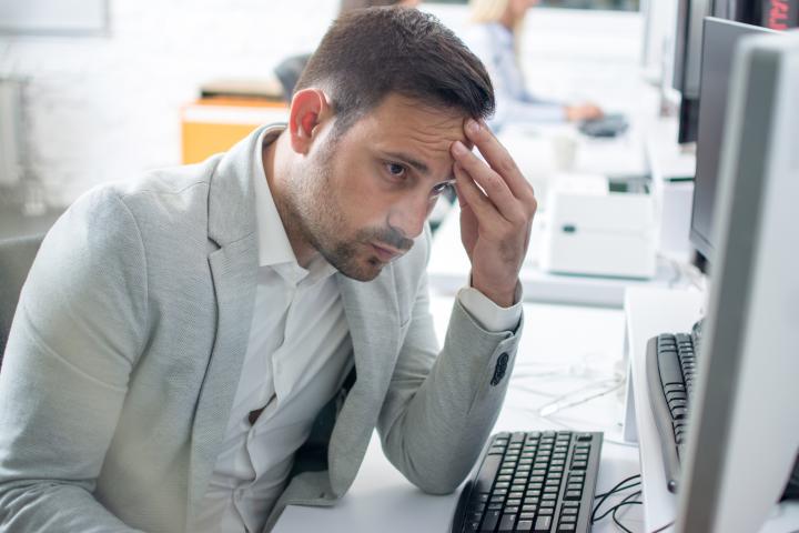 Empresario sufre dolor de cabeza mientras trabaja en el ordenador en la oficina