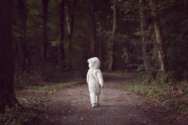 Niño pequeño con un traje de oso blanco, caminando por un sendero del bosque rodeado de árboles