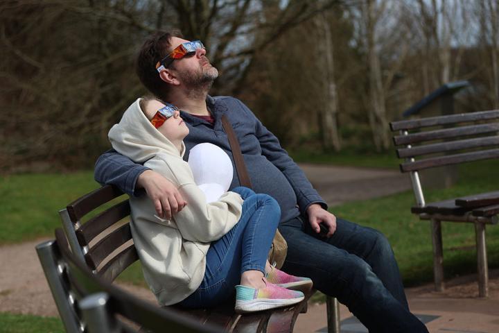 Un padre y su hija observan un eclipse solar con gafas protectoras en un parque.