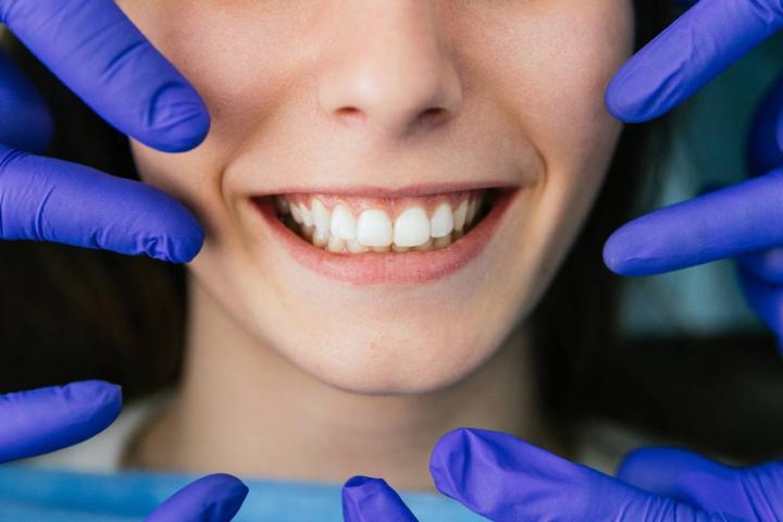 Primer plano de un dentista con guantes azules mostrando la dentadura perfecta de una joven que sonríe en la clínica dental.