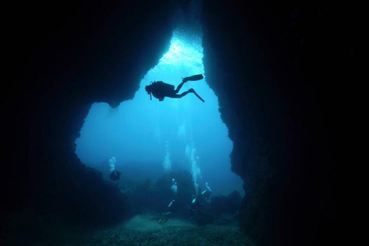 Buceadores con la silueta de una cueva al fondo, en Koh Ha Yai, provincia de Krabi, Tailandia