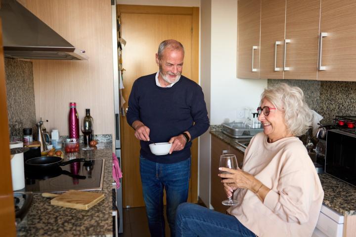 Dos personas mayores comparten un momento en la cocina de su piso en Valencia.