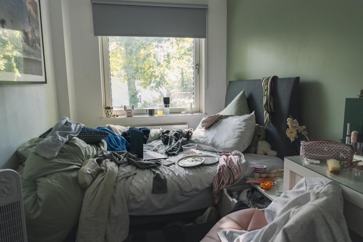 Un dormitorio desordenado, con la cama sin hacer, ropa descuidada y suciedad por todas partes.