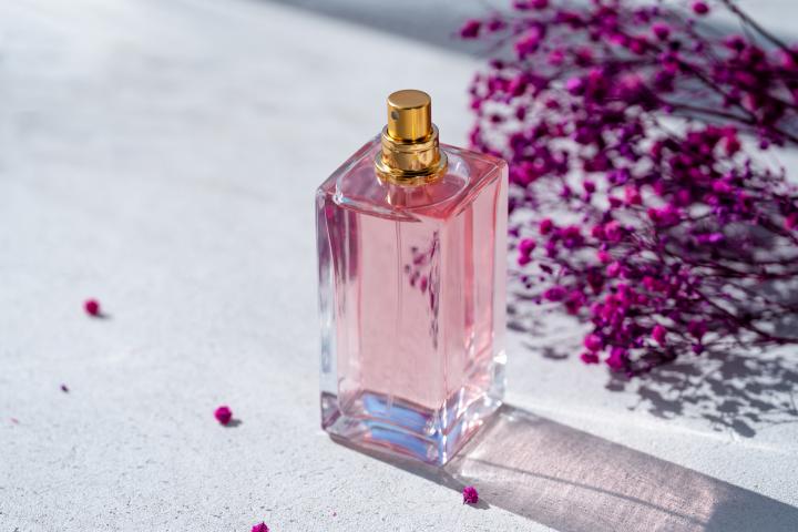 Un frasco de perfume de color rosa junto a unas flores