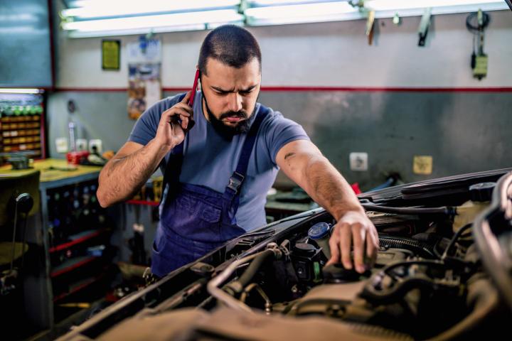 Mecánico frustrado haciendo una llamada mientras repara un automóvil en un taller mecánico