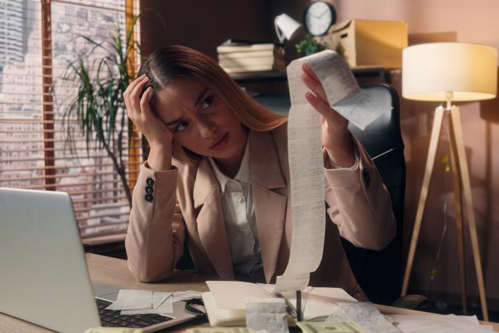 Mujer de negocios caucásica, preocupada, molesta y conmocionada, lee muchas facturas, un cheque grande, dinero en efectivo, crisis, bancarrota, impuestos, trabajo, computadora portátil en interiores. Video de alta calidad en 4K.