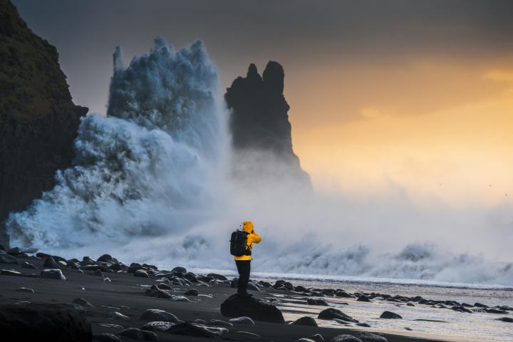 Explorador de pie en una costa rocosa con olas espectaculares y el atardecer como telón de fondo en Islandia.