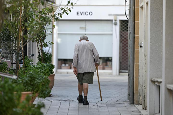 Un señor mayor caminando encorvado ayudado por su bastón