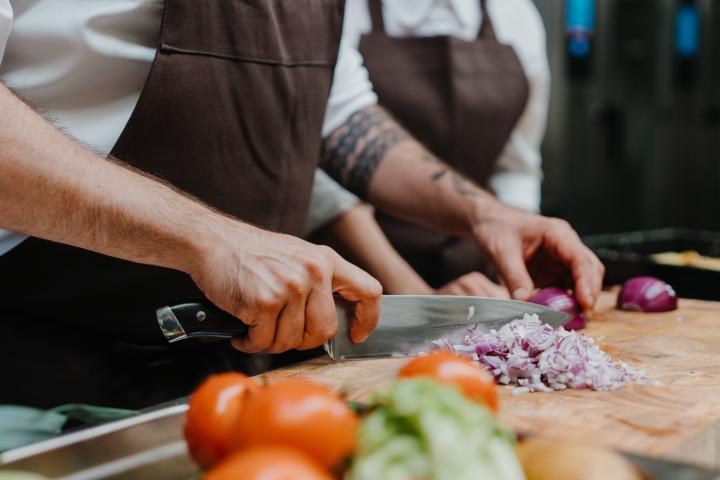Primer plano de un chef cortando cebolla sobre una tabla de cortar en la cocina de un restaurante. Cocineros profesionales picando verduras en un restaurante, con delantal de chef.