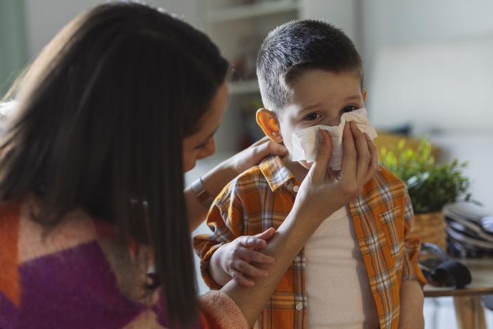 Mujer ayuda a niño a sonarse.