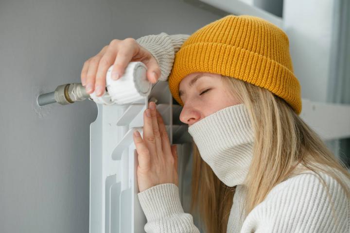 Mujer con sombrero calentándose mientras está sentada en el suelo cerca del radiador