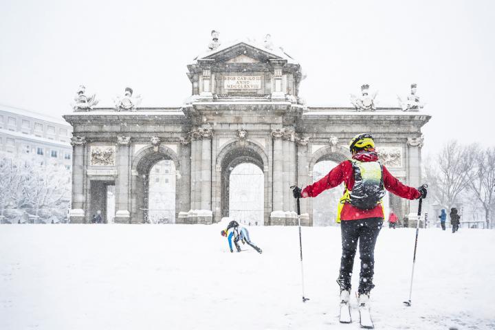 Hombre y mujer esquiando sobre la nieve frente a la Puerta de Alcalá durante la tormenta Filomena en 2021 en Madrid, España